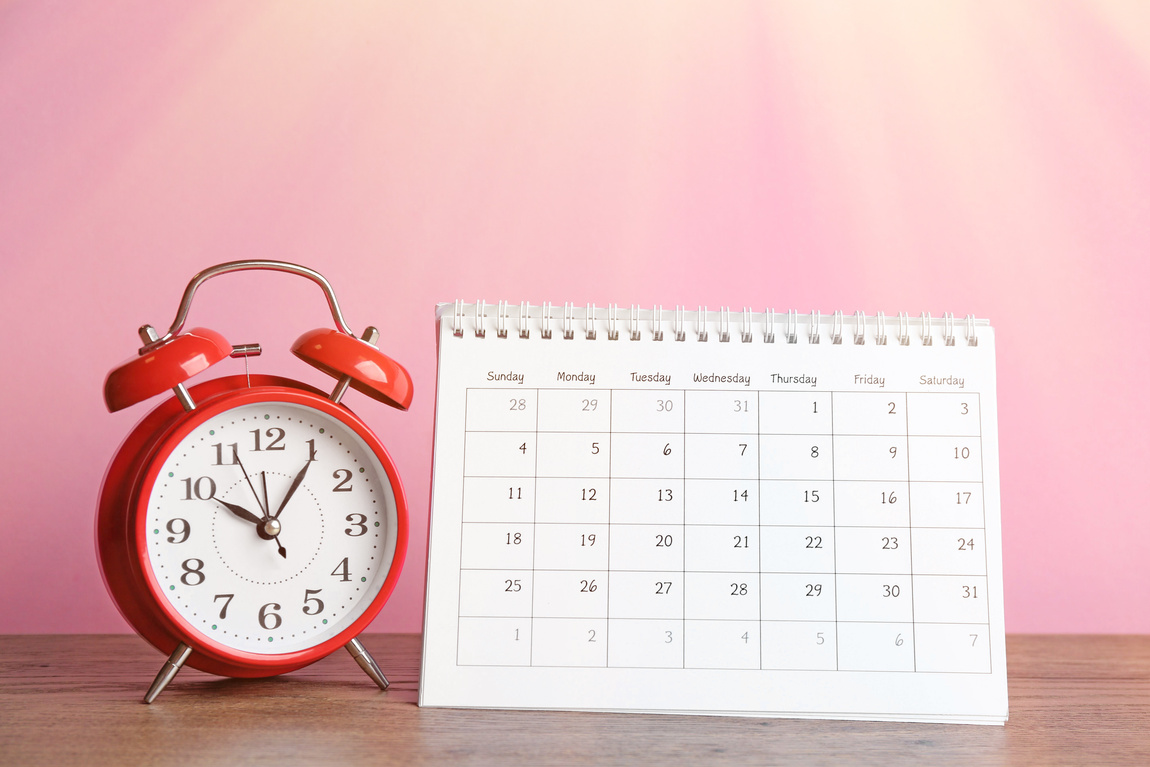Calender and Alarm Clock on Wooden Table against Pink Background